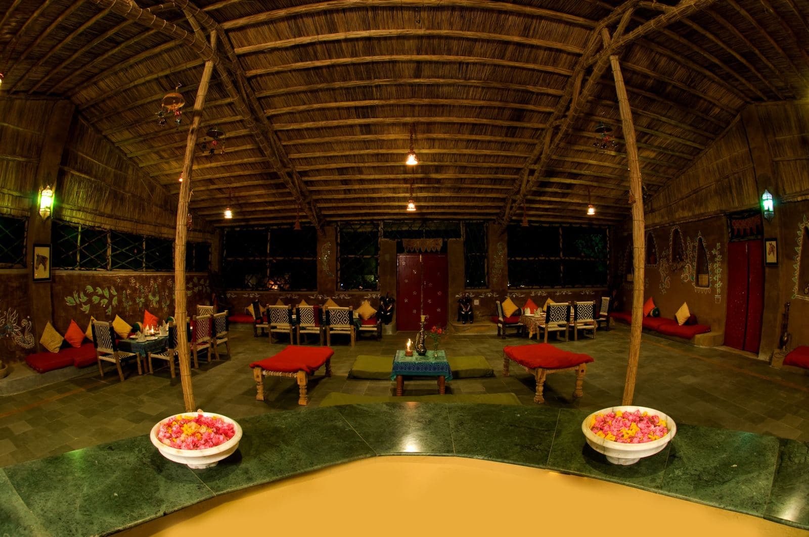 Warm-lit Indian dhaba dining room with low tables and flower bowls